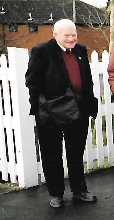 John Barber standing on a station platform, hands in pockets, sporting a cheeky smile.