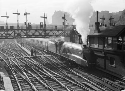 Streamlined A4 steam locomotive below a multi-track signal gantry leaving Edinburgh station