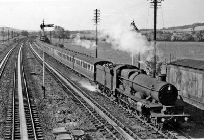 Steam locomotive on a passenger train takes on water from troughs in a countryside location