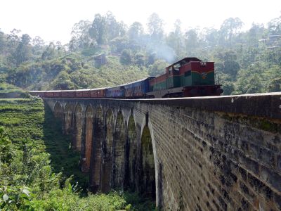 diesel-hauled passenger train on substantial stone viaduct in lush mountainous landscape