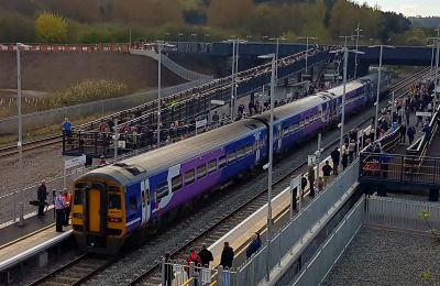 Modern railway station with two straight platforms. Hundreds of people are watching a four-car purple train.