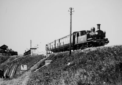 0-4-4T steam locomotive on 2-coach passenger train at a small halt station high up a grassy embankment