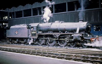 Former LMS Class 5 4-6-0 44949 at Manchester Victoria station, 1968 – Phil Sangwell. (CC BY-SA 2.0 – Flickr via Wikimedia Commons) A 1968 view of a grimy black 4-6-0 steam locomotive (an LMS Black Five) resting in the shadow of Manchester Victoria station's forbidding black wooden walls.