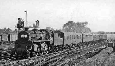 May 1964 picture of a 5-coach train being hauled by a steam locomotive on a suburban main line railway.