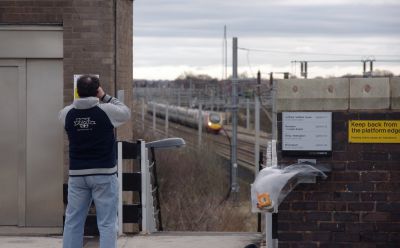 Man taking a photo of a distant Virgin Pendolino train from the vantage point of a station overbridge