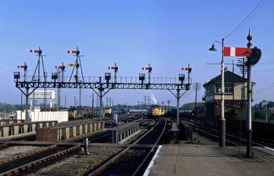 A view from the end of a railway station in 1971: an extensive semaphore signal gantry spans four tracks, framing several BR Rail Blue diesel locomotives in the distance.