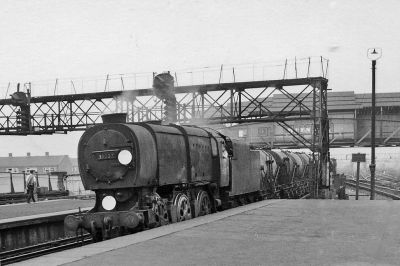 Archive view of an austerity-design steam locomotive, a Bulleid Q1, hauling a train of milk tank wagons through a large inner-city station in London.
