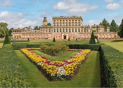 Cliveden House from the Parterre showing the restored 19th-century planting scheme A formal garden featuring triangular beds of colourful flowers, surrounded by precisely-cut hedges, with an extensive Victorian stately home in the background.