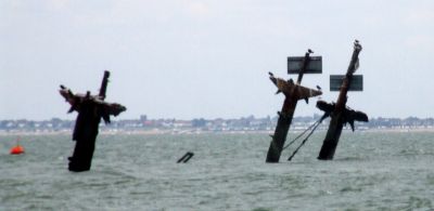 Three steel masts sticking up at a slight angle out of the grey waters of the Thames estuary.