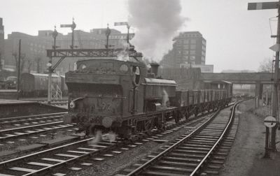Kensington Olympia station in 1968: London Transport pannier tank locomotive L.92 heads for Lillie Bridge Depot with a short engineer's train after night work on the District line. The ex-GWR 57xx class 0-6-0 loco (formerly 5786) has since been preserved. – User:8474tim – Wikimedia Commons (Public Domain) A short train of 4-wheel engineering wagons being hauled though an inner-city station by a London Transport steam locomotive in 1968.