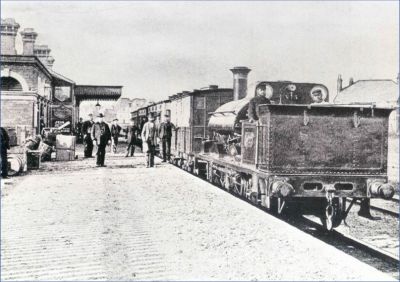 Marlow station during the 1870's, soon after the opening of the line. GWR 517 Class 0-4-2, in early saddle tank form, sits at the head of a passenger train. – Marlow Society website Victorian era view of Marlow station. An open-cab saddle tank steam locomotive sits at the head of a train of 4-wheel coaches. The station building features ornate brick chimneys, a short valanced canopy over the platform, and decorative stonework. A pile of boxes, barrels and other luggage is at the back of the platform. Seven gentlemen, in various uniforms and almost certainly all station staff, stand stiffly and some distance apart for the benefit of the photographer.
