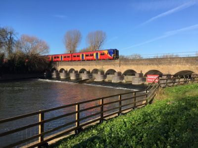 A brightly coloured multiple unit train crossing a multi-arched Victorian brick viaduct over a broad watercourse in the countryside.