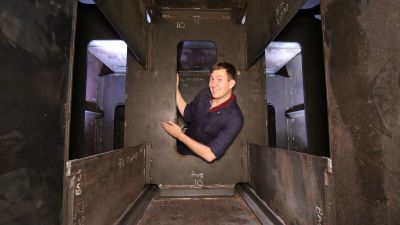 Inside the tender of BR Standard Class 4 75079, while filming an episode on how a steam locomotive works. (courtesy Will Stratford) A smiling gentleman in a boiler suit leans through a tall rectangular hole inside a boxy steel-fabricated structure (the inside of a steam locomotive tender).