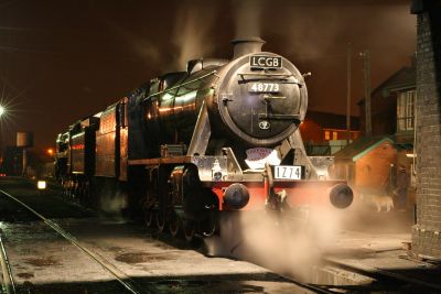 A heritage railway loco shed at night. A large heavy freight locomotive is in steam and being prepared for the next day's service.