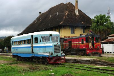 A Michelin railcar at Fianarantsoa, the inland end of the Madagascan Government-run line down to Manakara on the southeast coast. (2012) – (Colin Miell) A rural station scene in Madagascar. Either side of a very low, grass-covered platform stand two trains: in front is a vintage Michelin railbus; behind is a diesel freight locomotive. In the background is a substantial early twentieth century station building with large hipped, tiled roof.