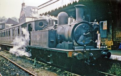 A Victorian steam locomotive at the head of a Victorian passenger train at a Victorian railway station, in run-down condition towards the end of steam on the Isle of Wight in 1965.