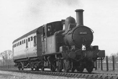 A small steam locomotive and single carriage (specifically: a GWR Class 14xx and auto-trailer) seen in flat countryside.