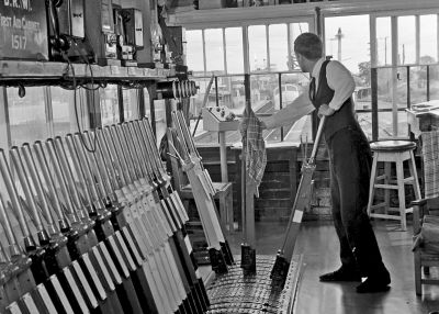David Canning working Thatcham Signal Box in 1974 Archive interior view of a mechanical signal box. The smartly uniformed signalman is at the lever frame looking away towards the train arriving at the station platform.