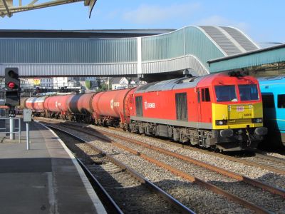 DB Class 60 No. 60020 passing Newport High Street station on the 0500 Robeston to Westerleigh Murco oil tanks – April 2014 – Brian Ringer A boxy diesel locomotive hauls a train of bogie oil tank wagons through a modern passenger station in South Wales.