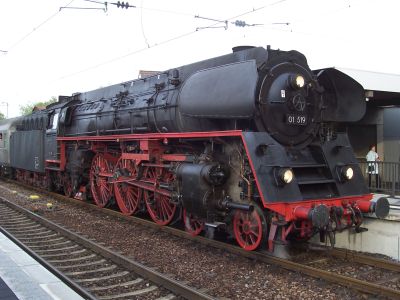 A large German steam locomotive in the distinctive livery of all-over black with bright red highlights on the wheels, motion and running plate.