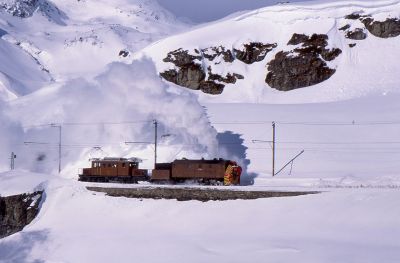 Steam Snow Blower Xrot 9213 assisted by Benina Line krokodil number 182, at Ospizio Bernina, Switzerland. Most winters the Rhatische Bahn run (expensive) excursions to photograph the snow blower in action. – 18 February 2018 – Neil Kearns Across the side of a snow-covered mountain, runs an electric railway. The masts and wires are highly visible against the virgin snow. A vintage Swiss Crocodile loco helps propel an even more vintage steam-powered snow blower to clear drifts from the track.