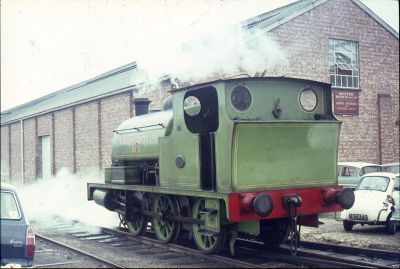 Slough Estates No.3 pauses between duties outside Weston's Biscuit Factory, sometime during the 1960s (P Jewell Collection) A small, green, 0-6-0 saddle-tank locomotive (Slough Estates No. 3) sits amid clouds of steam, near a brick factory building, surrounded by cars parked very close to the tracks.