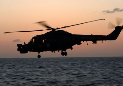 A Royal Navy Lynx helicopter, silhouetted against a sunset over a vast expanse of sea