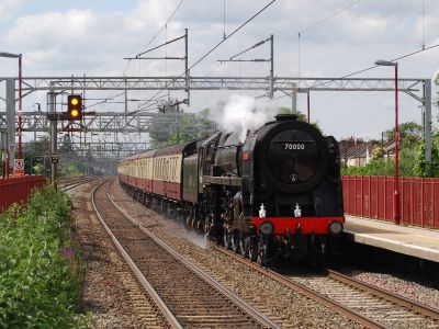 A large steam locomotive hauls a train of contemporary coaching stock through a suburban station.