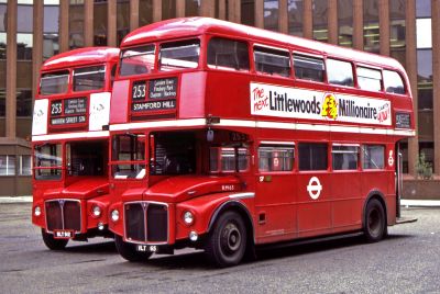 Two red London buses parked in front of a city office block.