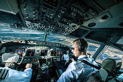 The cockpit of a Boeing 737 airliner, and its crew, with Europe just visible, far below, through the windows.