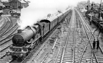 A monochrome view of the western approaches to Slough station on a Sunday in 1959. A large steam locomotive (a GWR 'Castle' class) heading west with an express passenger train to Plymouth on the down relief line. The fast lines on the right are being relaid.