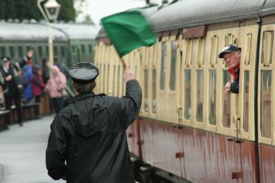 Busy station on heritage railway with guard waving green flag